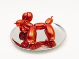 un chien en ballon rouge posé sur une assiette, sur une surface blanche