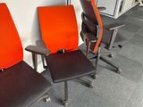 three orange and black office chairs are lined up against a white wall