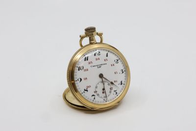 une petite montre de poche en or posée sur une surface blanche
