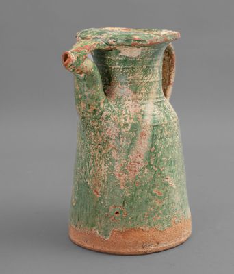 an old green vase with a handle on a gray surface