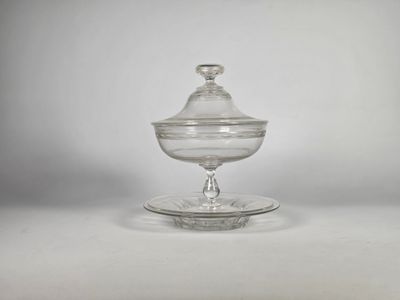 un saladier en verre transparent muni d'un couvercle, posé sur une assiette