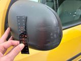 a person holding a measuring tape in front of a yellow car