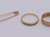 two gold rings and a pin are sitting next to each other