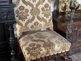 une chaise dont l'assise est recouverte d'un tissu à motifs floraux, à côté d'une table sur laquelle se trouve un vase de fleurs