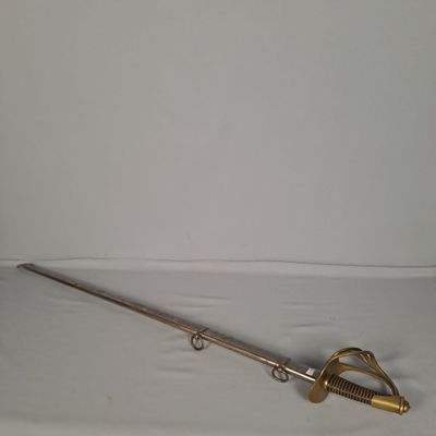 Une vieille épée repose sur une surface blanche, près d'un mur blanc.