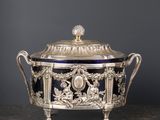 un plat à couvercle ancien, en argent et en verre bleu, posé sur une table