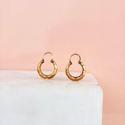 une paire de boucles d'oreilles créoles en or posée sur un bloc de marbre