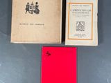 Trois livres sont posés sur une table ; l'un d'entre eux a une couverture rouge.