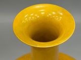 a yellow vase sitting on a table with a gray background