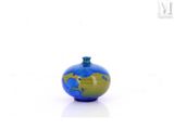 un petit vase bleu et vert posé sur une surface blanche