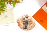 a watch sitting in a box on a table next to a plant