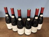 six bottles of wine are lined up on a wooden table