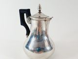 a silver coffee pot with a black handle on a white surface