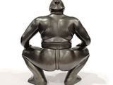 statue of a man sitting on a stool with his hands on his knees