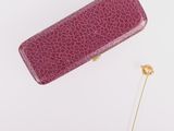 étui en cuir violet orné d'une broche dorée sur fond blanc