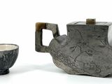 two teapots and a cup on a white surface