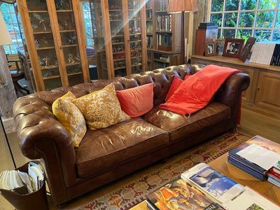 un canapé en cuir marron dans un salon où se trouvent de nombreux livres sur la table