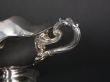 an antique silver gravy dish with a handle on a black surface