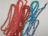 trois colliers de perles avec des pompons, posés sur un fond blanc