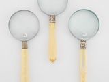 trois loupes posées sur une surface blanche, avec un manche jaune