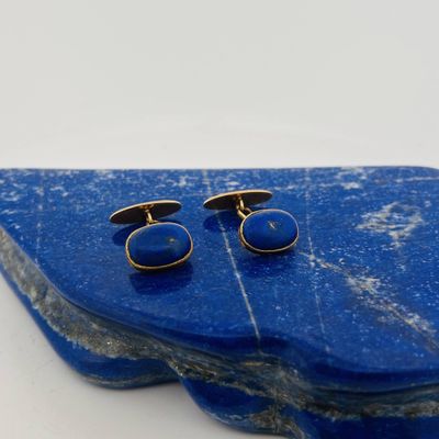 two pairs of blue and gold cufflinks on a blue rock