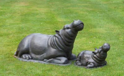 une statue représentant un hippopotame et son petit allongés dans l'herbe
