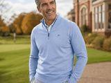 the man is standing in front of a large house wearing a blue sweater and grey pants
