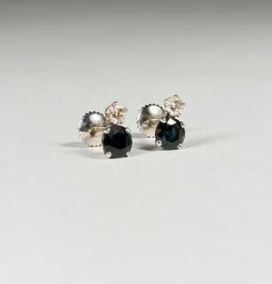 une paire de boucles d'oreilles à clous ornées de diamants noirs et blancs, posées sur une surface blanche