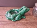 a green frog shaped ashtray sitting on a table next to a silver canister