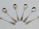 six cuillères en argent sont disposées en cercle sur une surface blanche