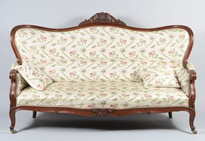 un canapé à l'ancienne, dont le dossier et les accoudoirs sont recouverts d'un tissu à motifs floraux