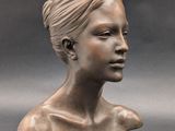 bronze sculpture of a woman ' s head on a gray background