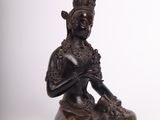 bronze statue of a woman sitting on a rock with her hands crossed