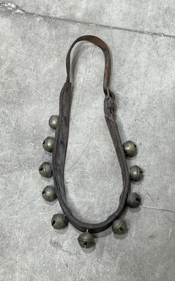 une photo d'un collier en cuir orné de clochettes posé sur un sol en béton