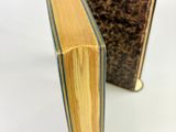 an old book sitting on top of a white table next to a smaller book