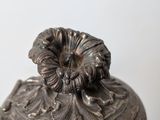 an antique silver metal container with a flower decoration on top