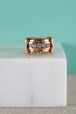 un gros plan d'une bague en or et diamants posée sur un bloc de marbre blanc