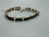 un bracelet noir et argenté orné de perles carrées sur fond blanc