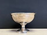 an antique silver plated bowl on a pedestal against a black wall