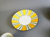 une assiette jaune et blanche accrochée au mur, à côté d'une tasse
