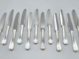 six silverplated knives and six knives on a white surface