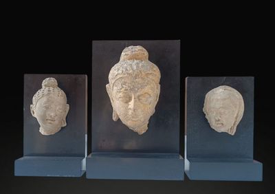 three stone heads of buddhas on display on a black background