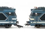 two blue trains sitting side by side on a white surface