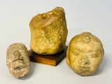 deux têtes en pierre et un visage en pierre posés sur un socle en bois
