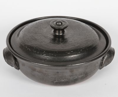 une casserole noire avec un couvercle, posée sur une surface blanche