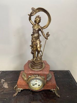 statue en laiton représentant une femme tenant une horloge posée sur une table en bois