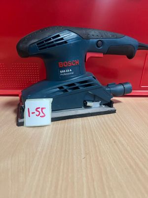 un gros plan d'une ponceuse filaire posée sur une table, avec une boîte rouge en arrière-plan