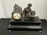 une statue représentant un homme assis sur un banc à côté d'une horloge