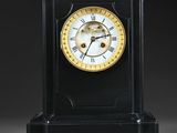une horloge noire avec un cadran doré, posée sur un socle
