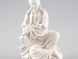 une statue blanche représentant une femme assise sur un rocher